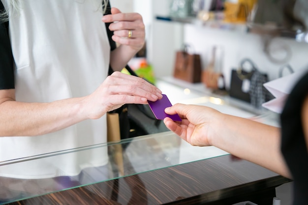 Free photo female customer paying for purchase by credit card in clothes store, giving blank card to cashier over desk. cropped shot, closeup of hands. shopping or purchase concept