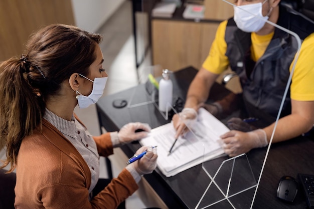 Cliente di sesso femminile con maschera protettiva per la firma di documenti presso l'officina di riparazioni auto