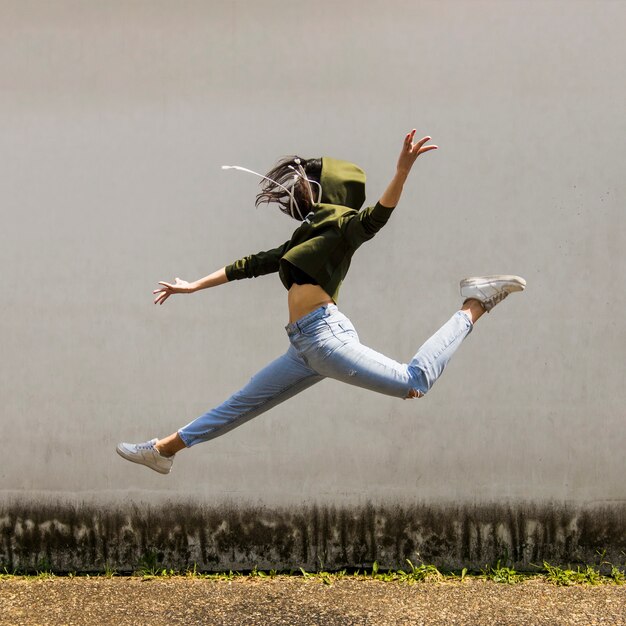Female dancer in hood jumping against wall