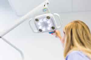 Бесплатное фото Женский стоматолог, регулирующий медицинскую лампу в клинике