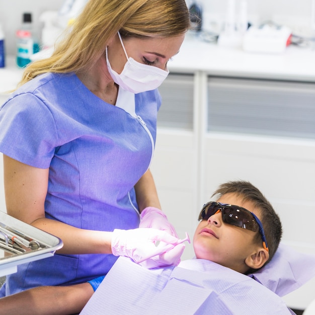 Female dentist checking boy's teeth with dental mirror