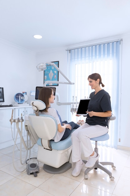 환자는 병원에서 의자에 앉아 디지털 태블릿 화면을 가리키는 여성 치과 의사