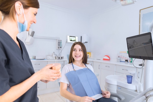 웃는 환자에게 치아 모델을 보여주는 여성 치과 의사