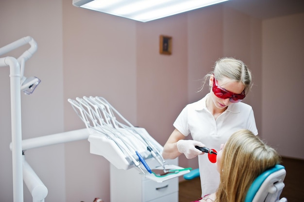 Female dentist in special red glasses treating her patient's teeth with dental instruments