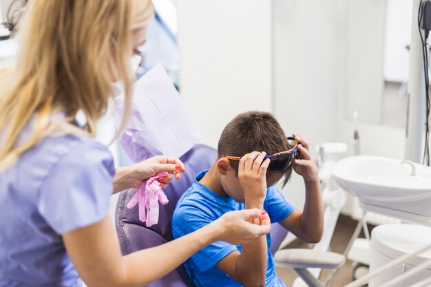Female dentist standing near boy removing safety protective glasses