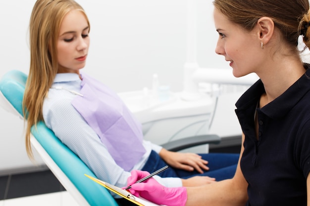 Female dentist talks with client about treatment holding papers in her arms