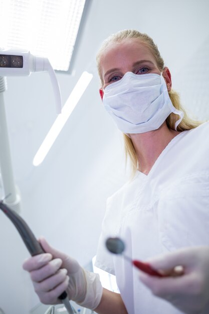 Female dentist with surgical mask holding dental instruments