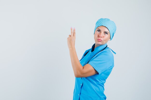 Female doctor in blue uniform gesturing with hand and fingers and looking confident , front view.