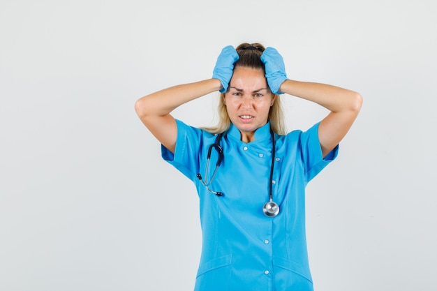 Free photo female doctor in blue uniform, gloves holding head with hands and looking disappointed