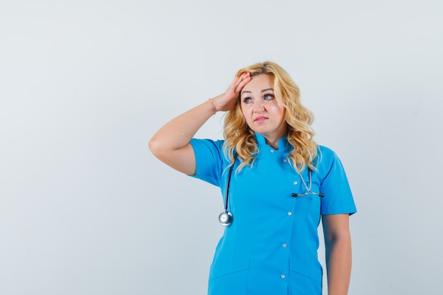 Женщина-врач в синей форме держит руку на голове, глядя в сторону