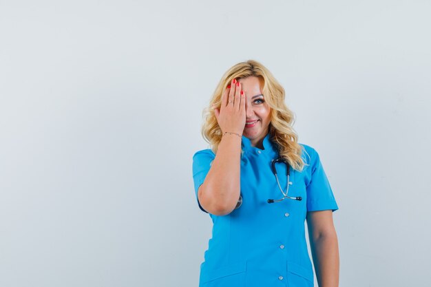 Female doctor in blue uniform holding hand on her half face and looking jolly space for text