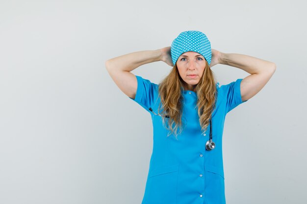 Female doctor in blue uniform holding hands behind head and looking confident 