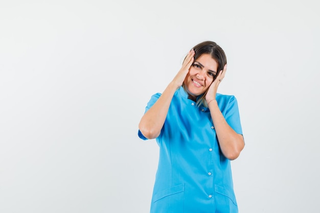 Female doctor in blue uniform holding hands to head and looking pretty