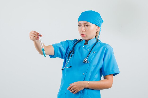 Female doctor in blue uniform holding test tube and looking surprised 