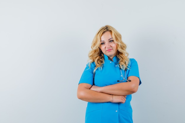 Foto gratuita dottoressa in uniforme blu tenendo le braccia incrociate e cercando pensieroso spazio per il testo