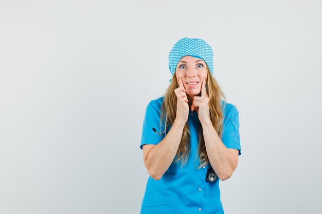 青い制服を着た女性医師が頬に指を保ち、陽気に見える