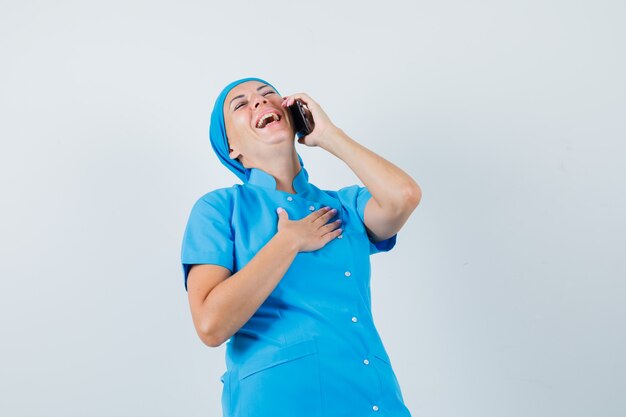 휴대 전화, 전면보기에 얘기하는 동안 웃 고 파란색 유니폼에 여성 의사.