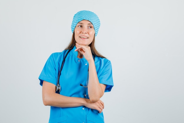 Female doctor in blue uniform looking away with hand on chin and looking hopeful