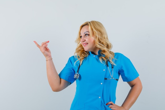 옆으로 가리키는 파란색 유니폼 여성 의사