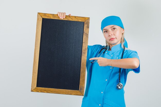 파란색 유니폼 칠판에 손가락을 가리키고 긍정적 인 찾고 여성 의사