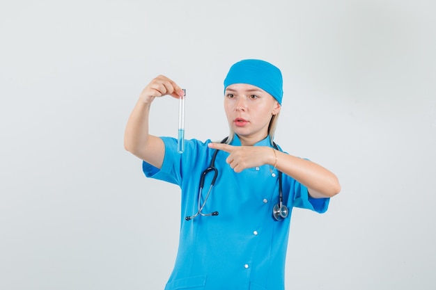 Female doctor in blue uniform pointing finger at test tube 