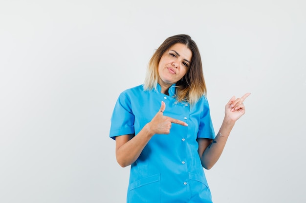 Female doctor in blue uniform pointing fingers away and looking confident