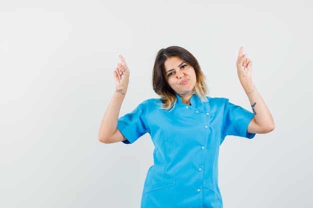 Female doctor in blue uniform pointing fingers up and looking confident