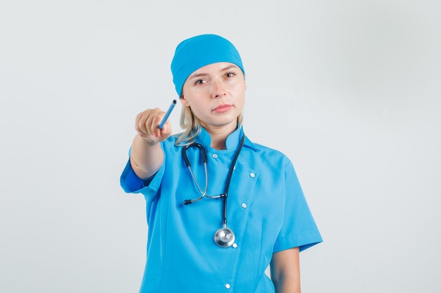 Female doctor in blue uniform pointing pencil to camera and looking careful 