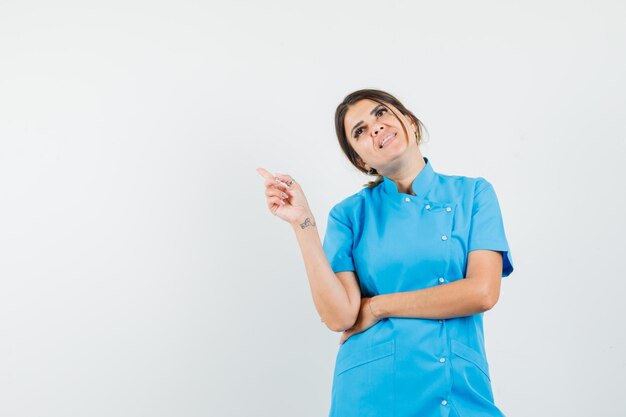 Female doctor in blue uniform pointing at upper left corner and looking hopeful