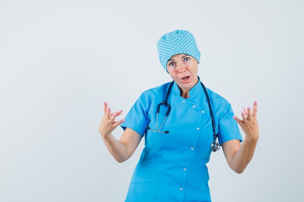 Female doctor in blue uniform raising hands in aggressive manner , front view.