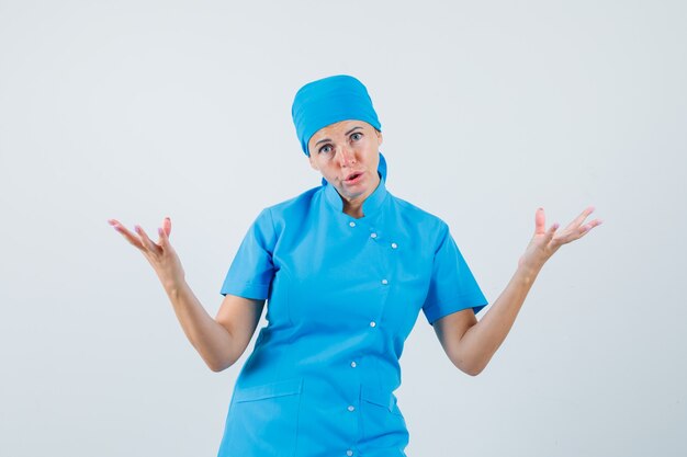 Female doctor in blue uniform raising hands in questioning manner and looking puzzled , front view.