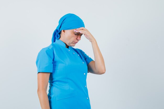 Free photo female doctor in blue uniform rubbing forehead and looking fatigued , front view.