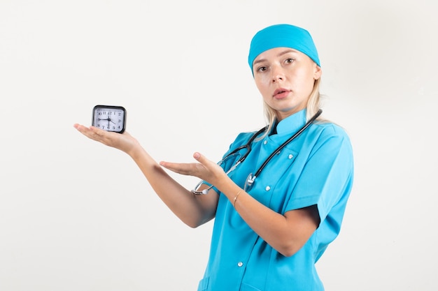 Foto gratuita dottoressa in uniforme blu che mostra all'orologio e guardando attento