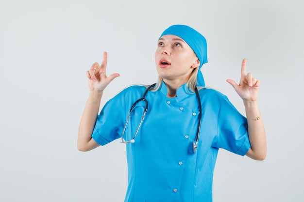 Female doctor in blue uniform showing gun gesture and looking up 