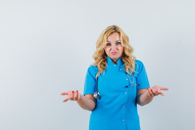 Женщина-врач в синей форме показывает беспомощный жест и выглядит встревоженной