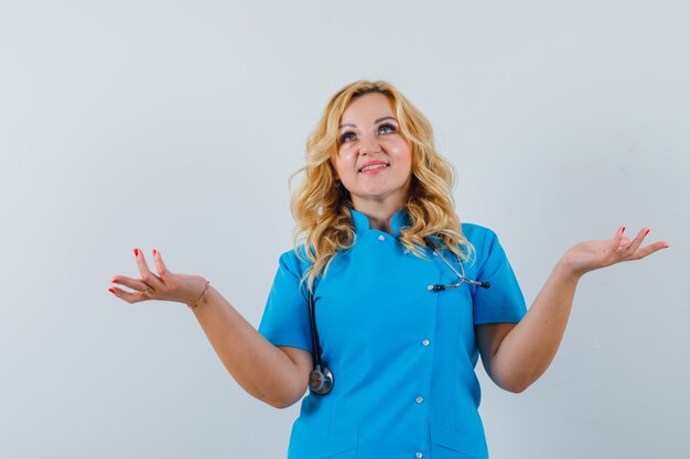 Female doctor in blue uniform showing helpless gesture and looking pleased