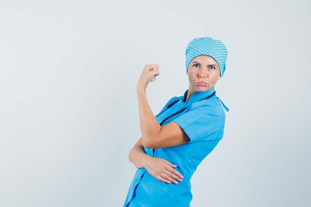 Female doctor in blue uniform showing muscles of arm and looking confident.
