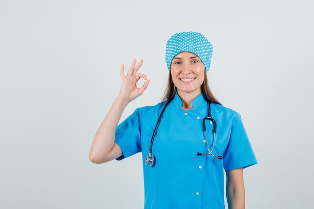 Female doctor in blue uniform showing ok gesture and looking cheerful