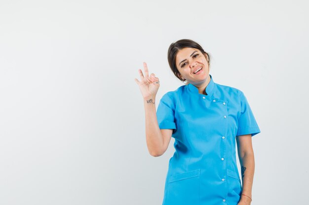 Female doctor in blue uniform showing ok gesture and looking merry