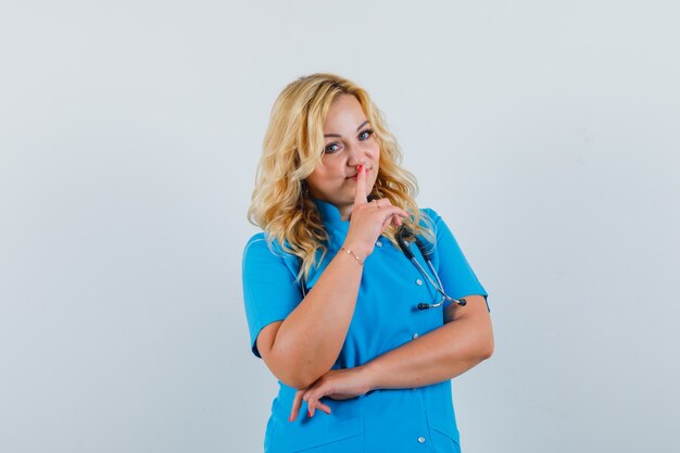 Female doctor in blue uniform showing silence gesture