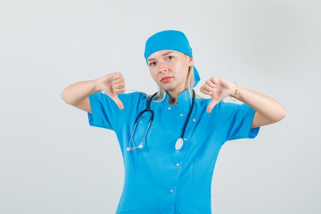 Female doctor in blue uniform showing thumbs down and looking disappointed 