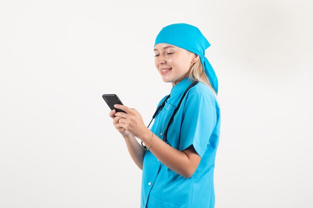 Female doctor in blue uniform smiling while typing on smartphone