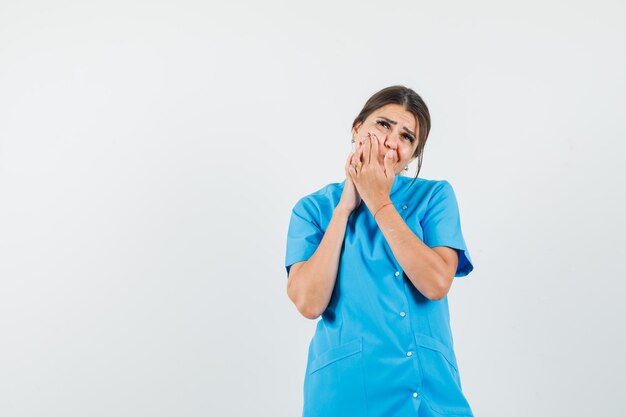 Female doctor in blue uniform squeezing pimple on cheek