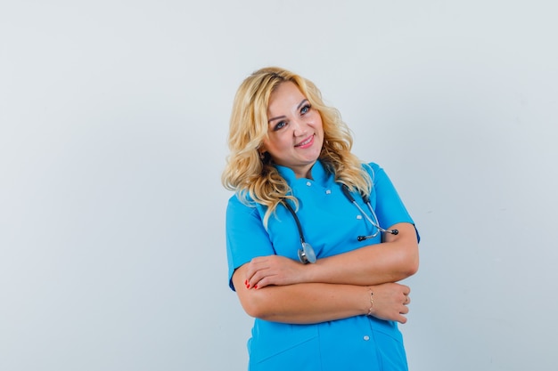 腕を組んで立って、テキストの幸せなスペースを探している青い制服を着た女性医師