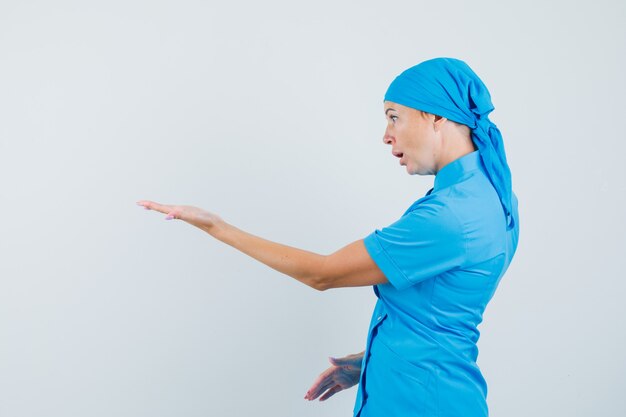 의아해 제스처에 손을 스트레칭 파란색 유니폼 여성 의사.