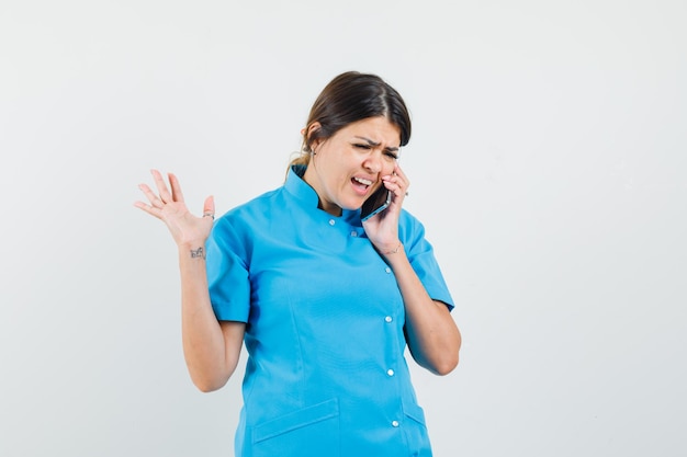 Female doctor in blue uniform talking on mobile phone and looking puzzled