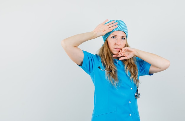 Female doctor in blue uniform touching head and face with hands 