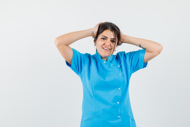 Female doctor clasping head with hands in blue uniform and looking pretty