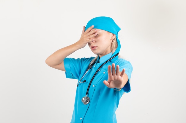 Free photo female doctor covering eyes while showing no gesture in blue uniform and looking scared