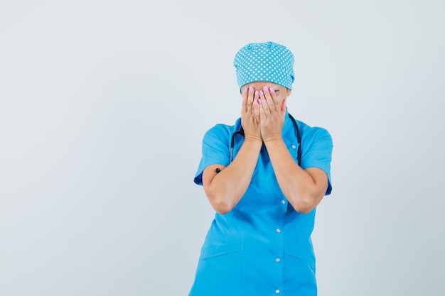 Medico femminile che copre il viso con le mani in uniforme blu e guardando sconvolto. vista frontale.